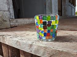 Zu sehen ist ein Glas, das rundum um mit bunten eckigen und runden Mosaiksteinen beklebt ist.